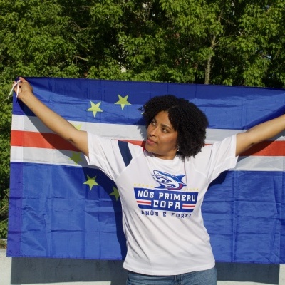 Pessoa segura bandeira azul com estrelas e riscas e veste t-shirt branca com estampado e texto