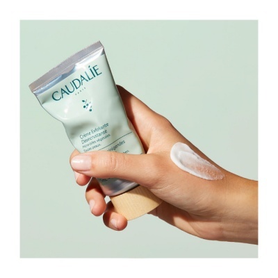 Mão a segurar tubo de creme esfoliante Caudalie com creme aplicado no dorso