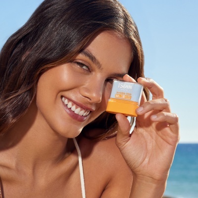 Mulher com protetor solar ISDIN SPF 50+ junto ao mar