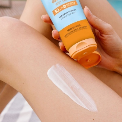 Mão segurando tubo de creme hidratante com proteção solar SPF 30 aplicando no braço