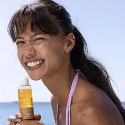 Frasco de creme solar VIS SPF 50 MOA segurado por mulher na praia