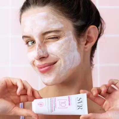 Mulher com máscara facial branca segurando creme SVR Sensifine AR [10]