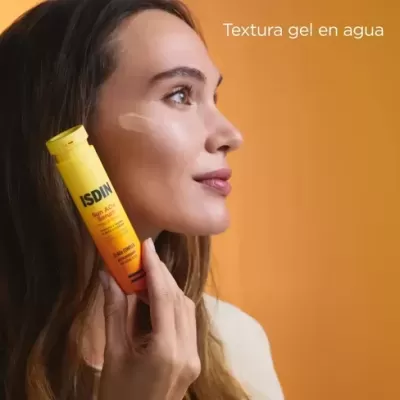 Mulher segura sérum solar ISDIN amarelo e laranja aplicando no rosto, fundo laranja com texto.