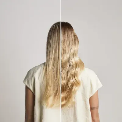 Mulher vista de costas com cabelo loiro dividido em metade liso e metade ondulado, utilizando blusa branca