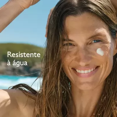Mulher aplicando creme no rosto à beira da praia com texto Resistente à água