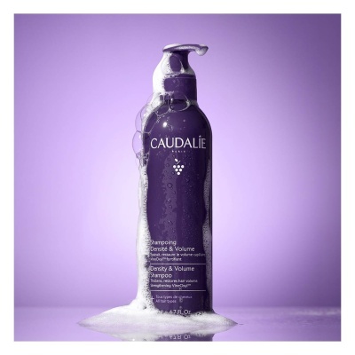 Frasco roxo de shampoo Caudalie com espuma e fundo roxo