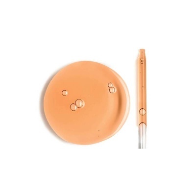 Base líquida bege claro com gotas de óleo e frasco translúcido