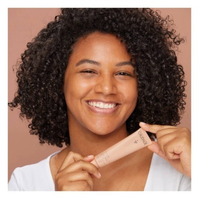 Mulher segurando tubo de creme CAUDALIE contra fundo cor de pele