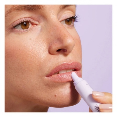 Mulher a aplicar produto labial com aplicador branco em fundo lilás