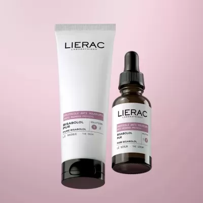 Dois produtos Lierac Bisabolol Pur, um tubo branco e um frasco âmbar com conta-gotas, com rótulos rosa claro, sobre fundo rosa.