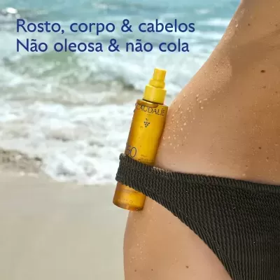 Frasco amarelo de protetor solar Caudalie SPF 50 preso ao fato de banho preto numa pessoa na praia