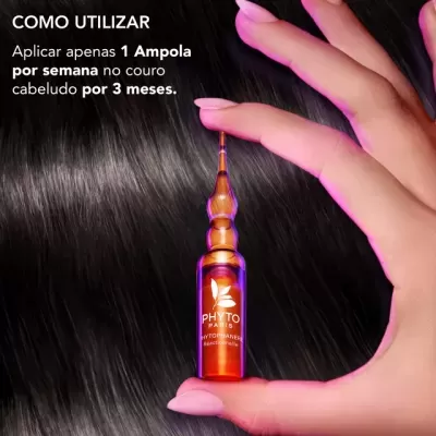 Mão a segurar ampola de vidro laranja PHYTO PARIS sobre cabelo preto brilhante com instruções de uso ao fundo