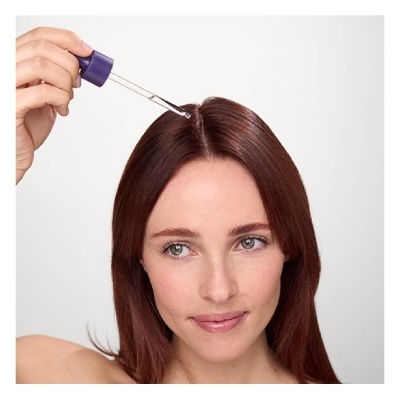 Mulher a aplicar líquido transparente no couro cabeludo com conta-gotas roxo