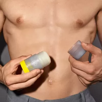 Desodorizante sólido em embalagem plástica com rótulo amarelo segurado por pessoa sem camisa