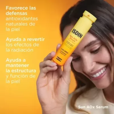 Frasco amarelo de sérum ISDIN Sun AOx Serum segurado por mulher sorridente com fundo laranja e texto em espanhol.