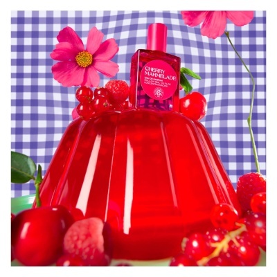 Frasco de perfume vermelho sobre gelatina vermelha com frutos e flores cor-de-rosa numa tela xadrez azul e branca
