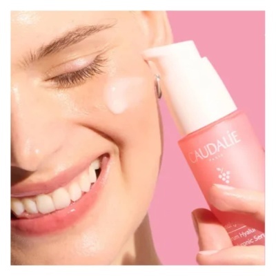 Mulher aplicando creme no rosto com frasco rosa Caudalie