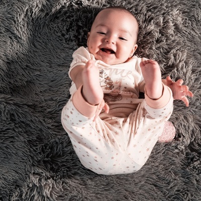 Bebé sorridente em pijama bege e rosa sobre almofada felpuda cinza