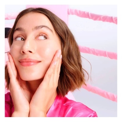 Mulher a tocar o rosto com as mãos, vestindo robe rosa.