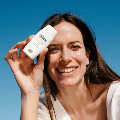 Mulher sorridente a segurar frasco de protetor solar ISDIN Fusion Water