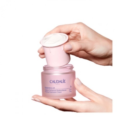 Frasco rosa de creme Caudalie segurado por duas mãos