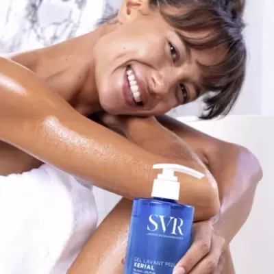 Frasco azul SVR Gel Lavant Peeling Xerial com doseador branco numa mão feminina