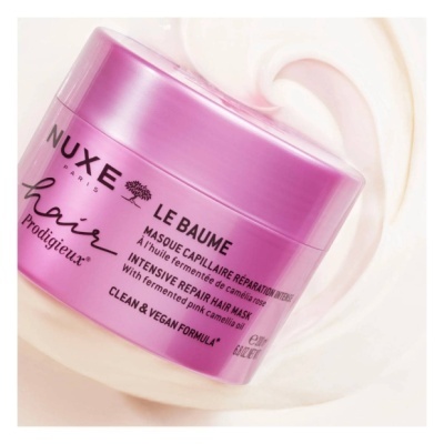 Frasco rosa metálico de máscara capilar NUXE LE BAUME hair Prodigieux sobre creme branco