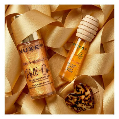 Produtos de beleza NUXE Roll-On e cuidado labial de mel com tampa de madeira, fitas douradas e acessório coração.