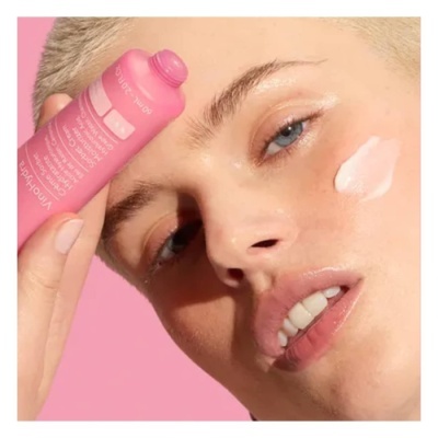 Pessoa com produto cosmético creme rosa na face e fundo rosa