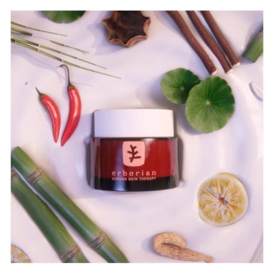 Frasco de creme Erborian rodeado por elementos naturais como paus de canela, folhas, malaguetas, bambu, limão e noz