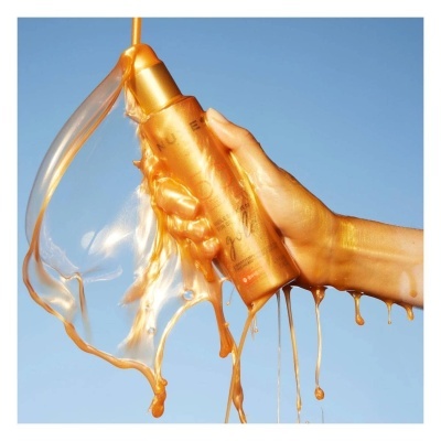 Mão a segurar garrafa dourada com líquido viscoso escorrendo