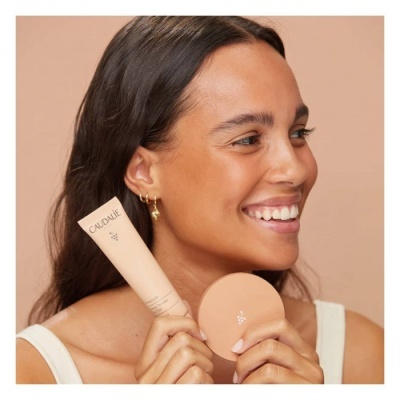 Mulher segura dois produtos cosméticos CAUDALIE em fundo neutro