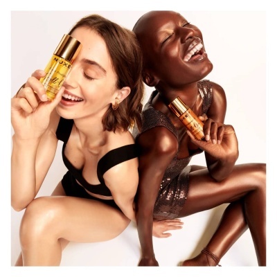 Duas mulheres sorrindo segurando frascos dourados de óleo NYX PROFESSIONAL MAKEUP