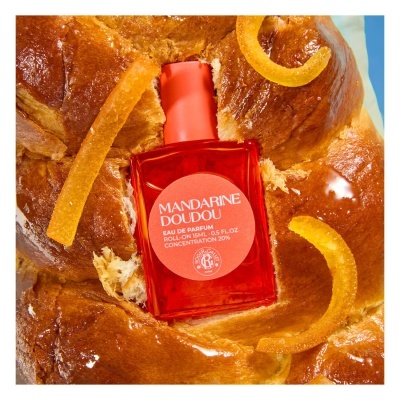 Frasco vermelho de perfume roll-on sobre pão doce com casca de laranja.