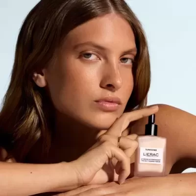 Frasco de cosmético LIERAC SUNISSIME ao lado do rosto de mulher com cabelo castanho.