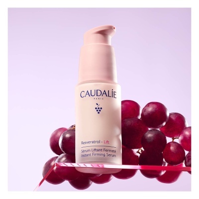 Frasco de sérum Caudalie com uvas vermelhas ao fundo