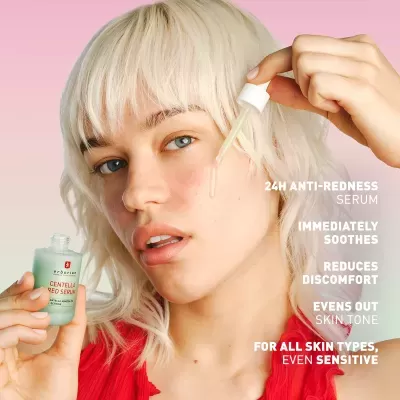 Mulher loira aplica sérum facial erborian Centella Red Serum com conta-gotas, fundo rosa e texto promocional em branco
