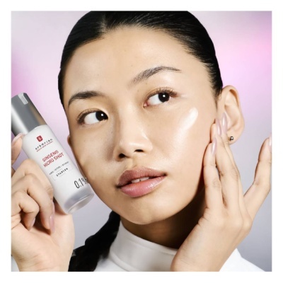 Mulher aplica creme no rosto segurando frasco de GINSENG MICRO SHOT da Erborian