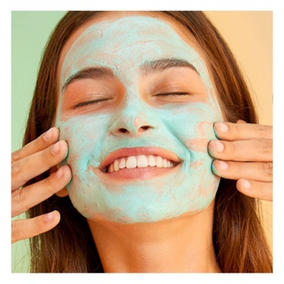 Mulher sorridente aplicando máscara facial verde clara no rosto