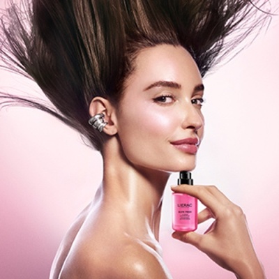 Mulher com pele luminosa a segurar frasco rosa de cosmético