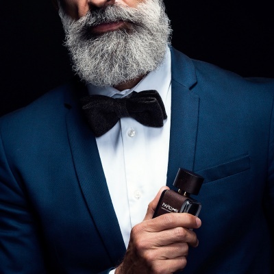 Homem com casaco azul e gravata borboleta segurando perfume