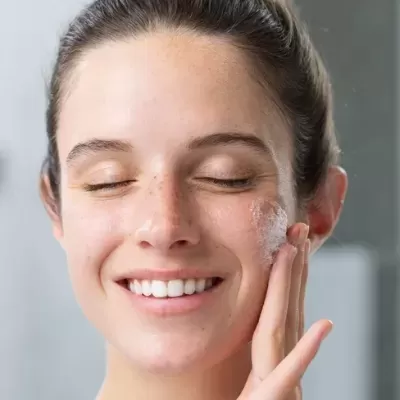 Mulher aplica creme ou espuma facial branca no rosto em ambiente interior