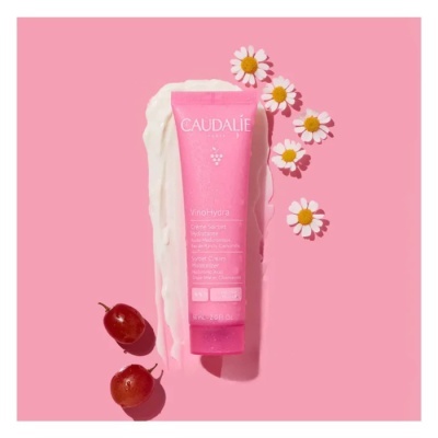 Tubo rosa de hidratante Caudalie Vinosource com flores e uvas sobre fundo rosa
