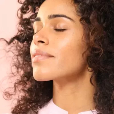 Mulher de cabelo encaracolado com olhos fechados e fundo rosa claro