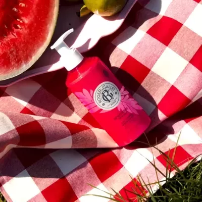 Frasco vermelho Roger & Gallet com tampa de bomba sobre toalha xadrez e frutas