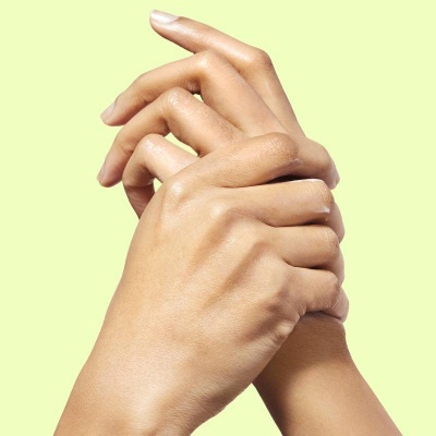 Duas mãos femininas entrelaçadas contra fundo amarelo claro