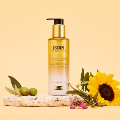 Frasco de limpeza facial ISDIN dourado com doseador, sobre pedra com azeitonas e flor amarela