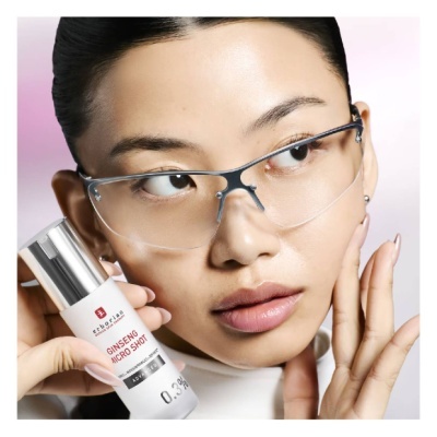 Frasco do produto GINSENG MICRO SHOT 0.3% com mulher de óculos prateados no fundo rosa e branco