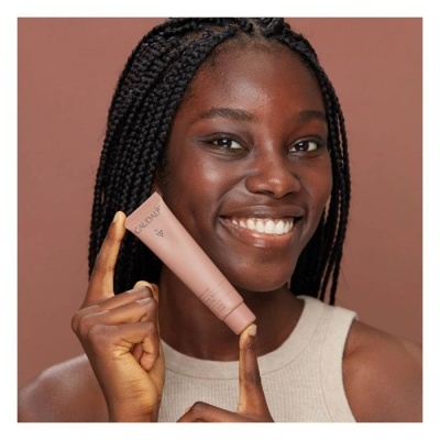 Mulher negra com cabelo trançado segurando tubo de produto Cosmétique CAUDALÍE em fundo castanho