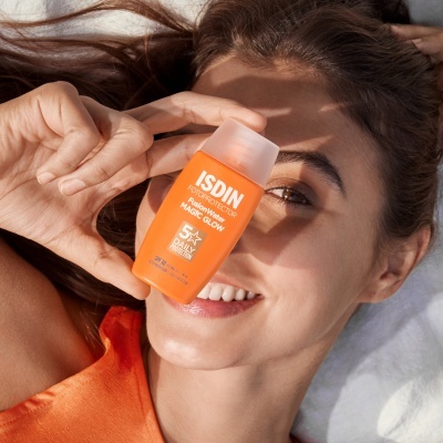 Frasco laranja de protetor solar facial ISDIN SPF 50+ segurado por mulher de pele clara deitada